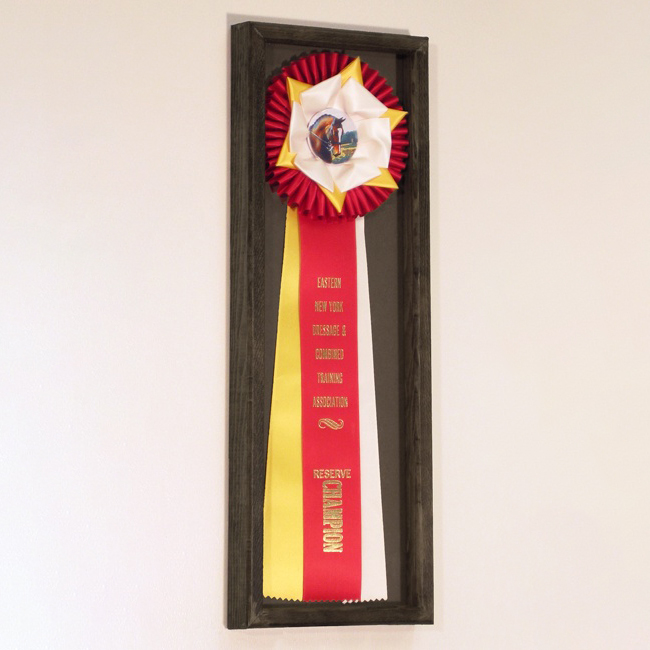 A rosette ribbon with longer streamers framed into a wooden box.