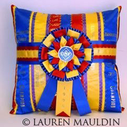 A decorative pillow made from the streamers of award ribbons with a single, large rosette with three streamers in the middle.