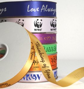 A stack of satin acetate continuous print ribbon rolls featuring different logos and messages.