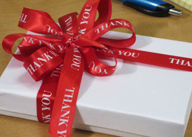 A gift wrapped in a red ribbon that reads Thank You, sitting on an office desk, used to stay socially connected to a team member.