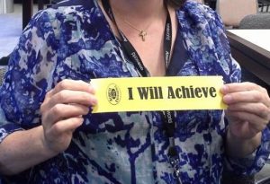 Woman holding a yellow "I Will Achieve" commitment ribbon.