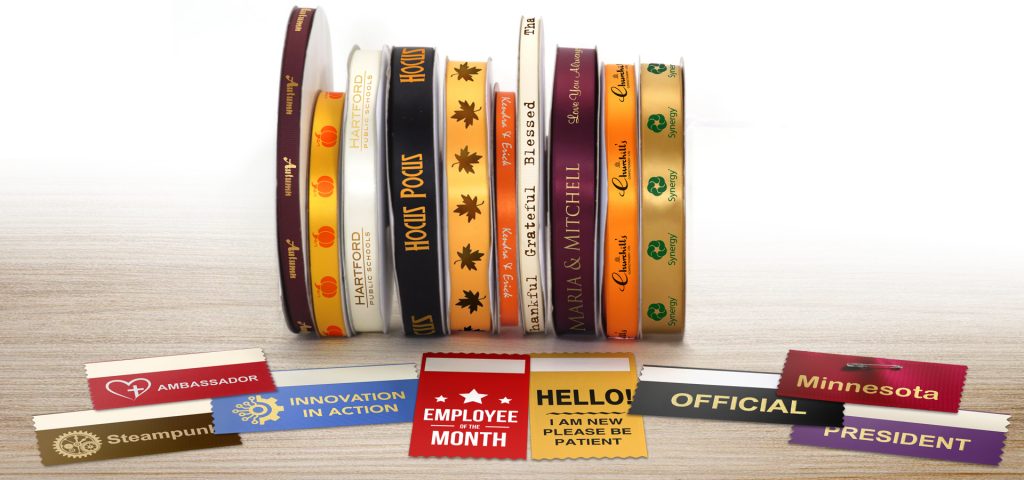A stack of ribbon rolls and several badge ribbons customized with imprinted logos, graphics and text all sitting on a table.